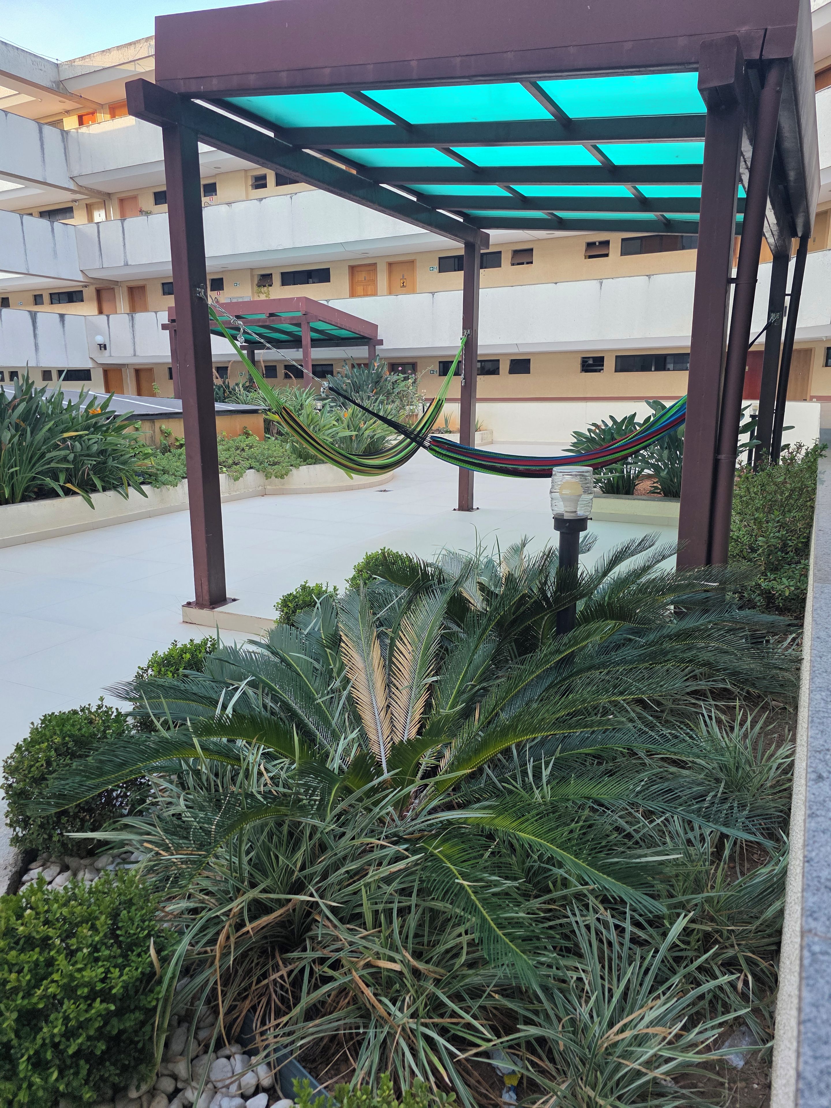 Área externa coberta com rede, plantas em vasos e um edifício ao fundo.