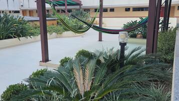 Área externa coberta com rede, plantas em vasos e um edifício ao fundo.