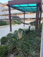 Área externa coberta com rede, plantas em vasos e um edifício ao fundo.