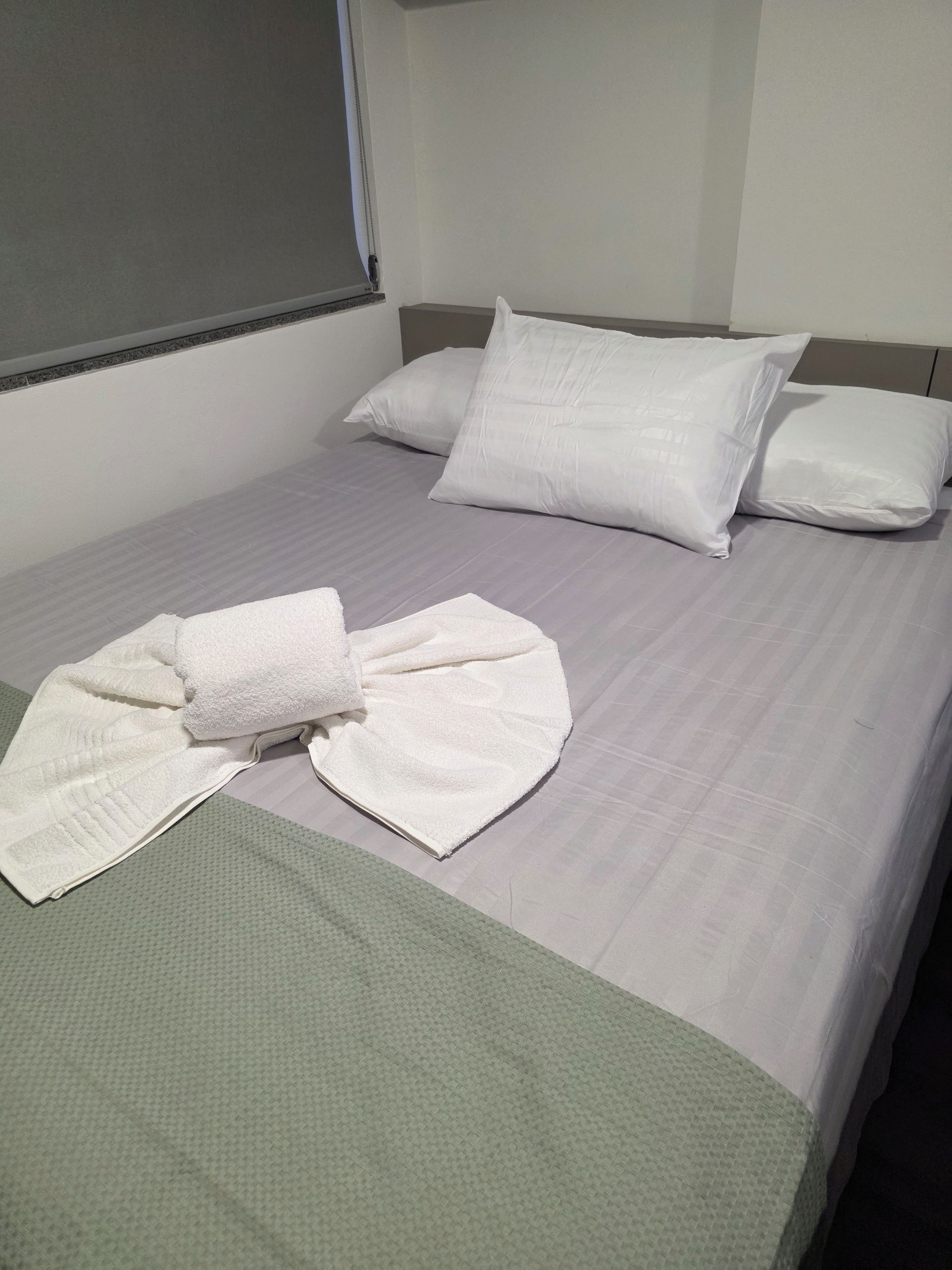 A hotel room with a bed, pillows, a folded towel, and a green blanket.