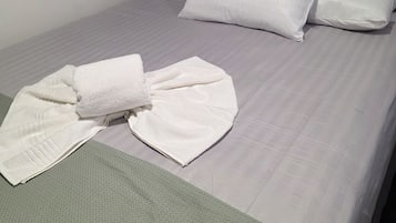 A hotel room with a bed, pillows, a folded towel, and a green blanket.