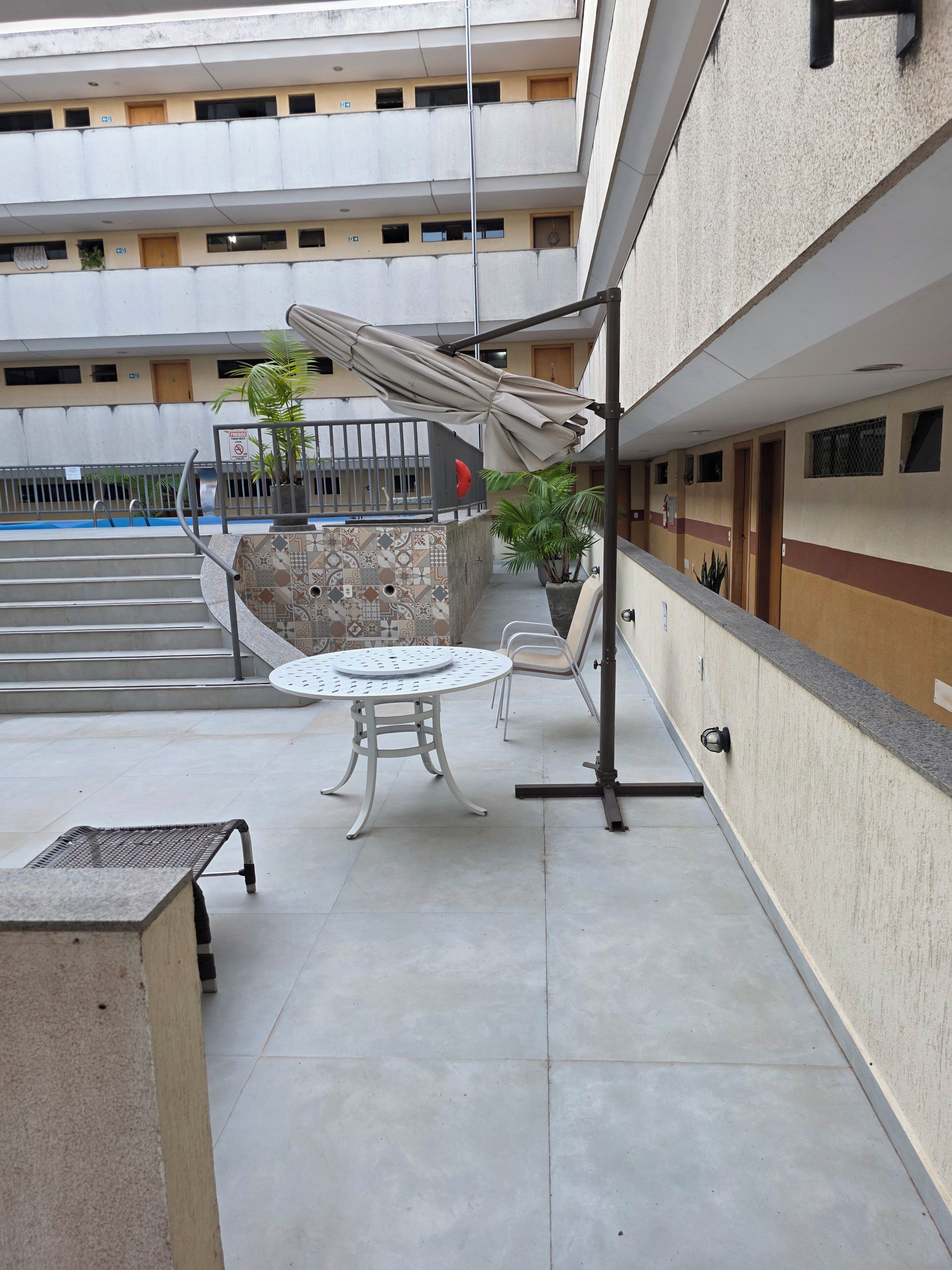 Um pátio com área de estar coberta, uma piscina pequena e uma escadaria que leva a um andar superior.