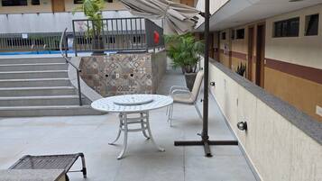 Um pátio com área de estar coberta, uma piscina pequena e uma escadaria que leva a um andar superior.