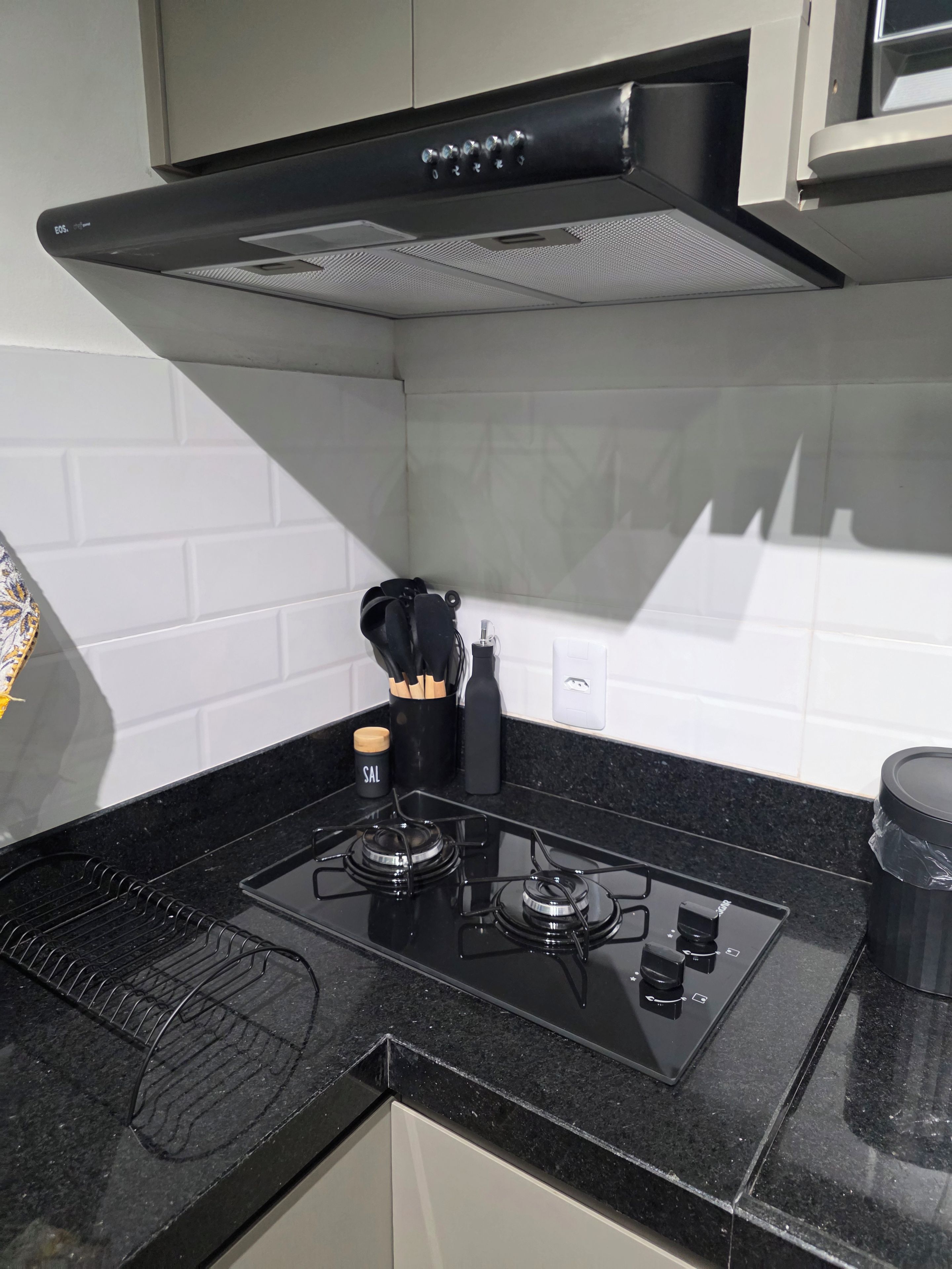 Cozinha com fogão preto, painel de azulejos brancos e exaustor preto.