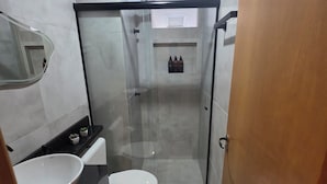 Un baño moderno con ducha envuelta en vidrio, lavamanos blanco y un inodoro.
