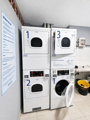 A laundry area with four washing machines, numbered 1 to 3, and a dryer. Instructions are posted on the wall.
