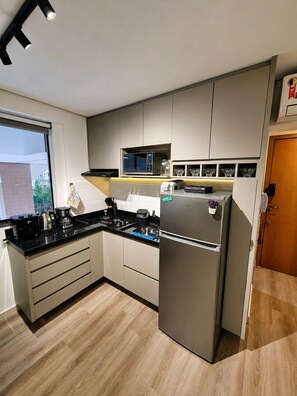 A modern kitchen with a built-in microwave, a stainless steel refrigerator, and a black countertop.