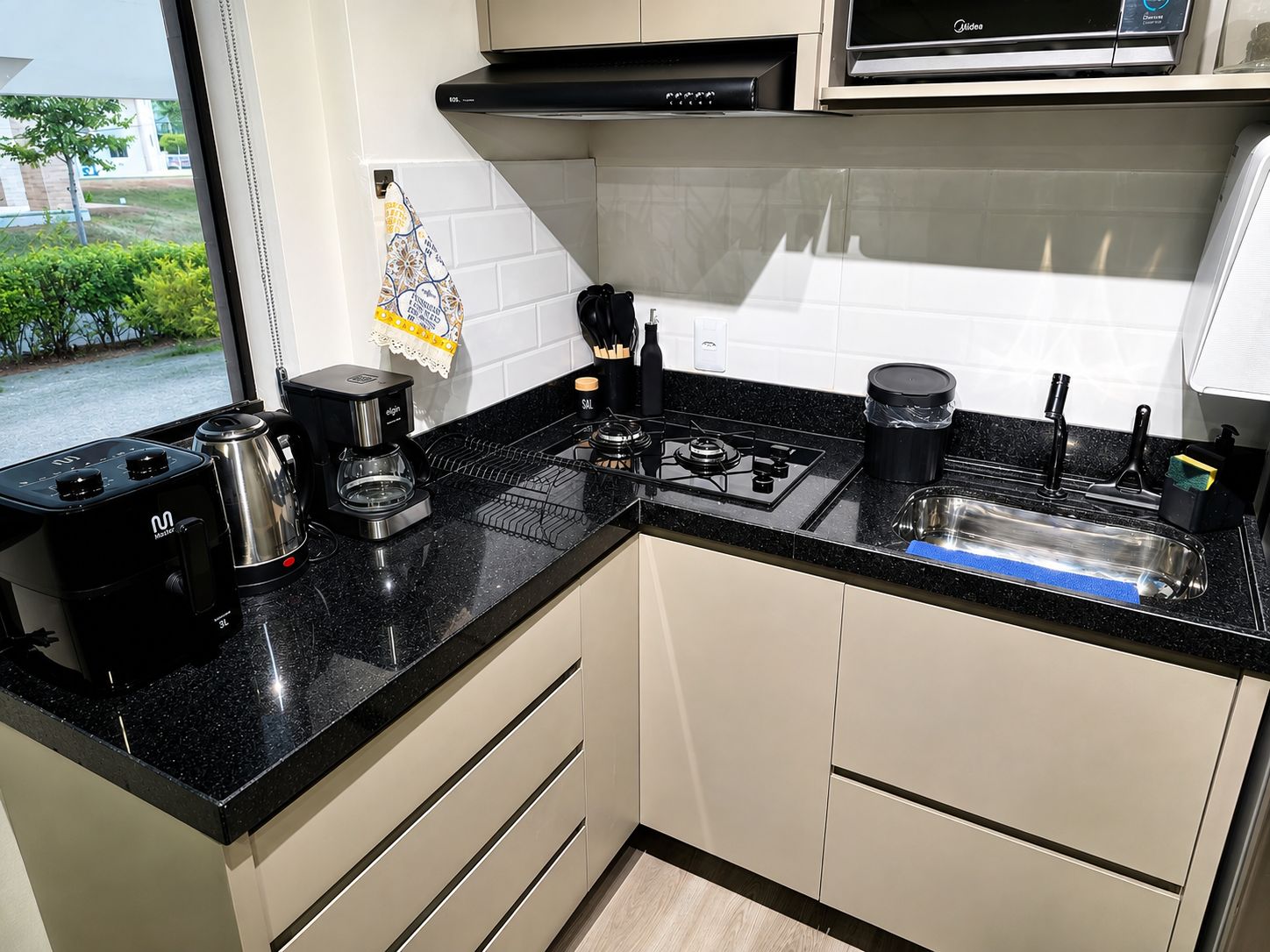 A modern kitchen with a gas stove, coffee maker, and a view of greenery outside.