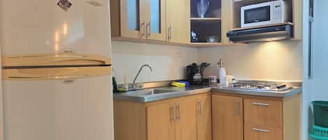A compact kitchen with wooden cabinets, a built-in microwave, and a refrigerator.