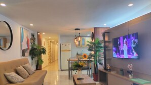 Una sala moderna con sofá, mesa de centro, televisor y cocina al fondo.