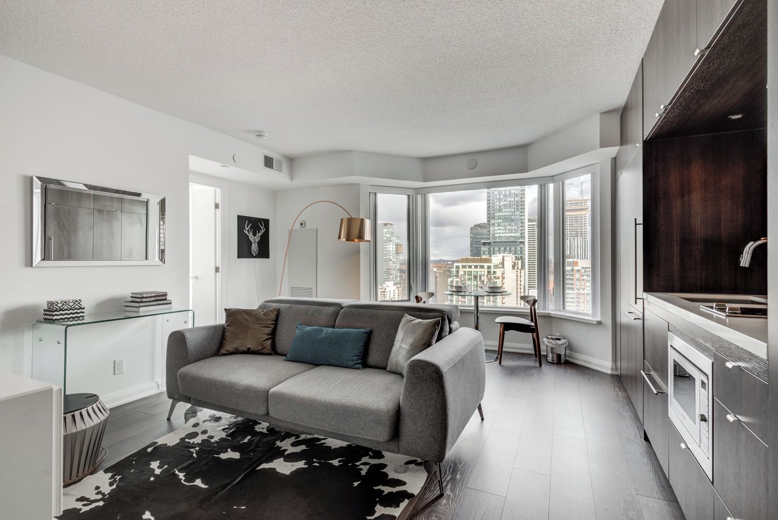 A modern apartment with a grey sofa, a glass coffee table, and a city view through large windows.