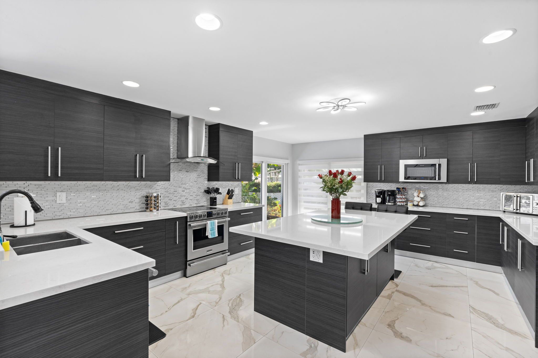 A modern kitchen with dark cabinetry, a central island, and a large window.