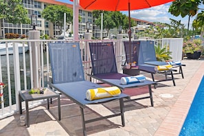A poolside area with lounge chairs, a table with a bottle, and a red umbrella. - Waterfront | Boat Rental | Heated Pool | Game Rm | Gym (Lighthouse Point)