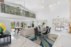 A spacious living area with a dining table, sofas, and a high ceiling with string lights. - Waterfront | Boat Rental | Heated Pool | Game Rm | Gym (Lighthouse Point)
