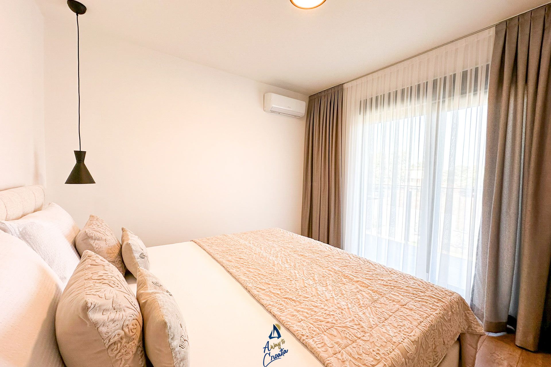 Une chambre d’hôtel avec un lit, des oreillers, une lampe suspendue, un appareil de climatisation et une fenêtre avec des rideaux.
