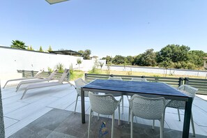 An outdoor patio area with a table and chairs, a white wall, and a view of trees and a building in the background. - 3-BR Villa with Private Pool Near the Beach (Zaton)