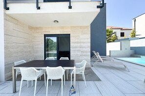 Eine Terrasse im Freien mit Tisch und Stühlen, einem Pool und einem modernen Gebäude im Hintergrund.