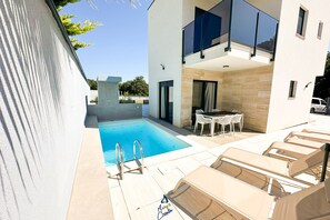 A modern outdoor pool area with a clear blue pool, a small table with chairs, and lounge chairs. - 3-BR Villa with Private Pool Near the Beach (Zaton)