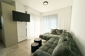 Ett modernt vardagsrum med en hörnsoffa, en platt-TV som är monterad på väggen och ett litet runt bord.