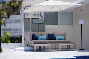 A modern outdoor seating area with a sofa, cushions, and a table, near a pool and a lamp. - Modern 2BR/2BA • Pool • Parking • Near Beach / Victoria Park / Las Olas (Fort Lauderdale)