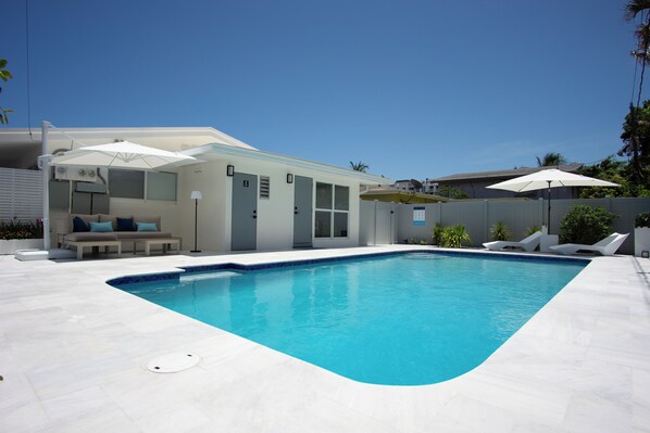 A modern pool area with a clear blue pool, white lounge chairs, and umbrellas. - Modern 2BR/2BA • Pool • Parking • Near Beach / Victoria Park / Las Olas (Fort Lauderdale)