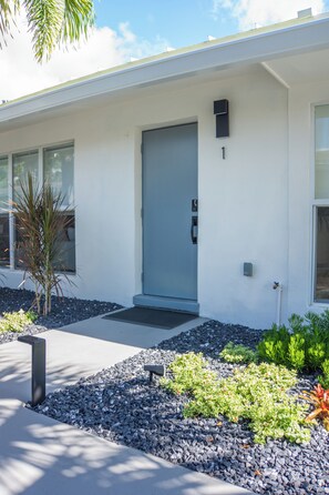 A modern building with a blue door, a small mailbox, and a well-maintained garden with various plants. - Modern 2BR/2BA • Pool • Parking • Near Beach / Victoria Park / Las Olas (Fort Lauderdale)