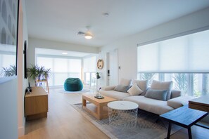 A modern living room with a sofa, coffee table, and a bean bag chair. There is a large window providing natural light and a view of the outdoors. - Modern 2BR/2BA • Pool • Parking • Near Beach / Victoria Park / Las Olas (Fort Lauderdale)