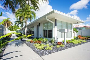 Una casa moderna de dos pisos con techo plano, ventanas amplias y un jardín cuidado con diversas plantas y un sendero.
