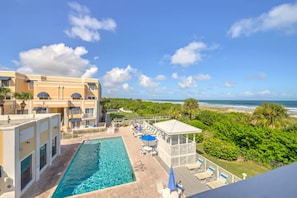 A hotel with a pool, lounge chairs, and a view of the ocean.