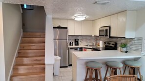 A modern kitchen with a central island, bar stools, stainless steel appliances, and a staircase leading to another level. - Amazing 2 /2 Beachside Get Away w/Nice Ocean View! (Cape Canaveral)