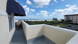 A balcony with a view of the beach and ocean, a chair, and a partial view of a building.