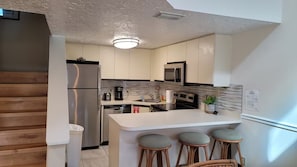 A modern kitchen with a central island, bar stools, stainless steel appliances, and a textured ceiling.