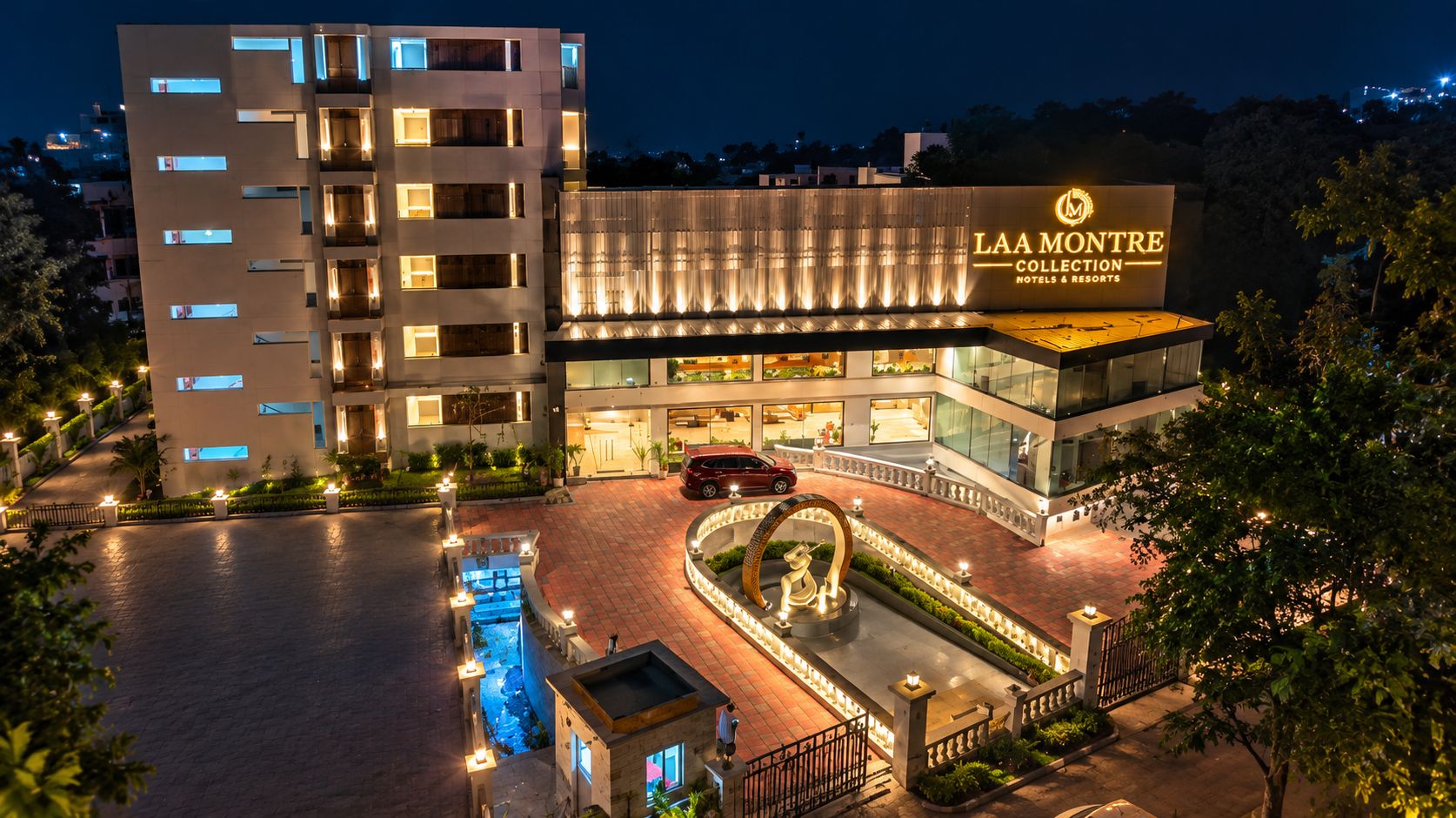 A multi-story hotel with a prominent entrance, a swimming pool, and a landscaped area with a statue.