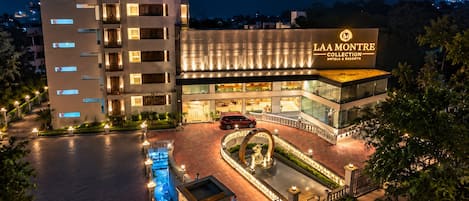 A multi-story hotel with a prominent entrance, a swimming pool, and a landscaped area with a statue.