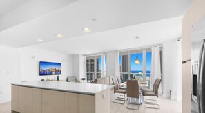 A modern kitchen with a central island, dining area with chairs, and large windows offering a view of the city skyline. - Beachwalk Resort Style 3BR Comfort Resort Vibes (Hallandale Beach)