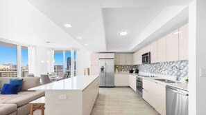 A modern kitchen with a central island, stainless steel appliances, and a view of the city. - Beachwalk Resort Style 3BR Comfort Resort Vibes (Hallandale Beach)