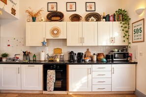 A kitchen with white cabinets, a black countertop, and various kitchen appliances. There are decorative items on the wall and a framed sign.