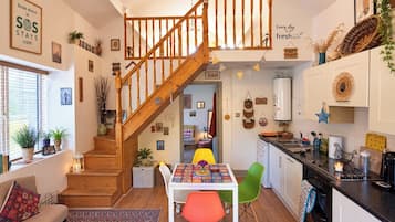 A cozy kitchen with a wooden staircase, a dining table with colorful chairs, and various kitchen appliances.