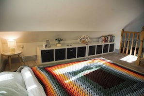 A bedroom with a bed, a bedside table with a lamp, a storage unit with cabinets, and a window allowing natural light.