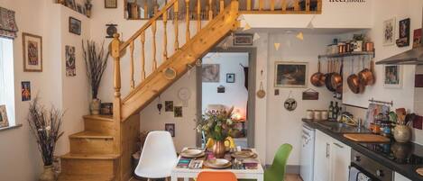 A cozy kitchen with wooden stairs, a dining table with chairs, and various kitchen utensils.