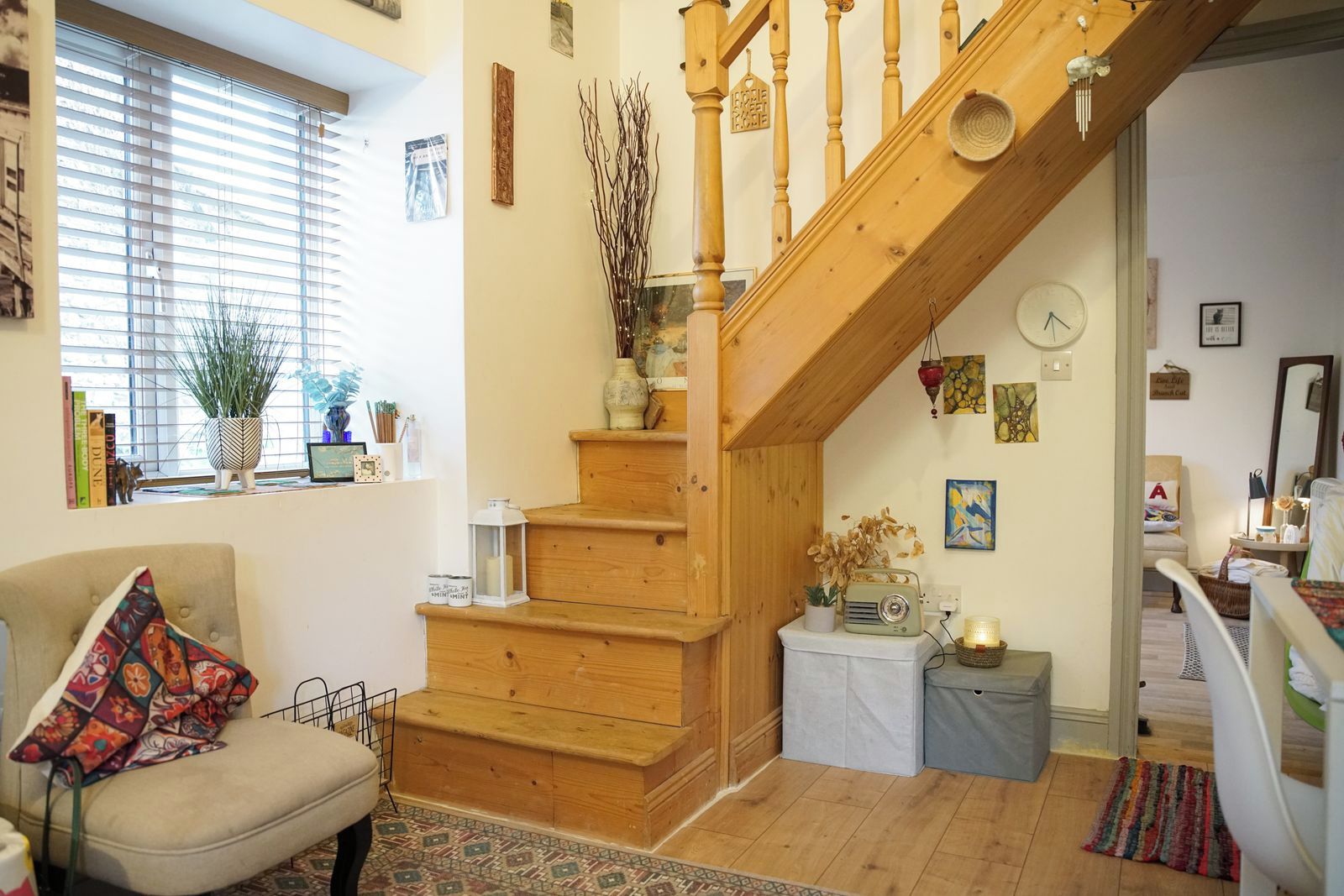 A cozy living room with a wooden staircase, a comfortable armchair, and a bookshelf.