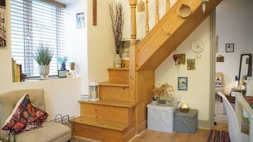 A cozy living room with a wooden staircase, a comfortable armchair, and a bookshelf.