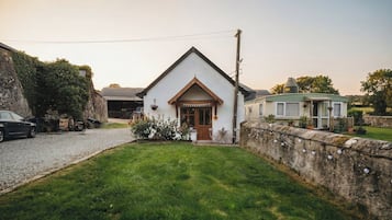 A white building with a pitched roof, a front door, and a small porch with a table and chairs.