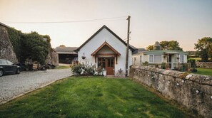 Un edifici blanc amb teulada inclinada, una porta principal i un petit porxo amb taula i cadires.
