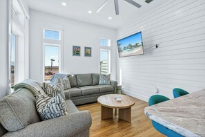 Una sala de estar moderna con un sofá gris, una mesa de centro redonda de madera y un televisor montado en la pared.