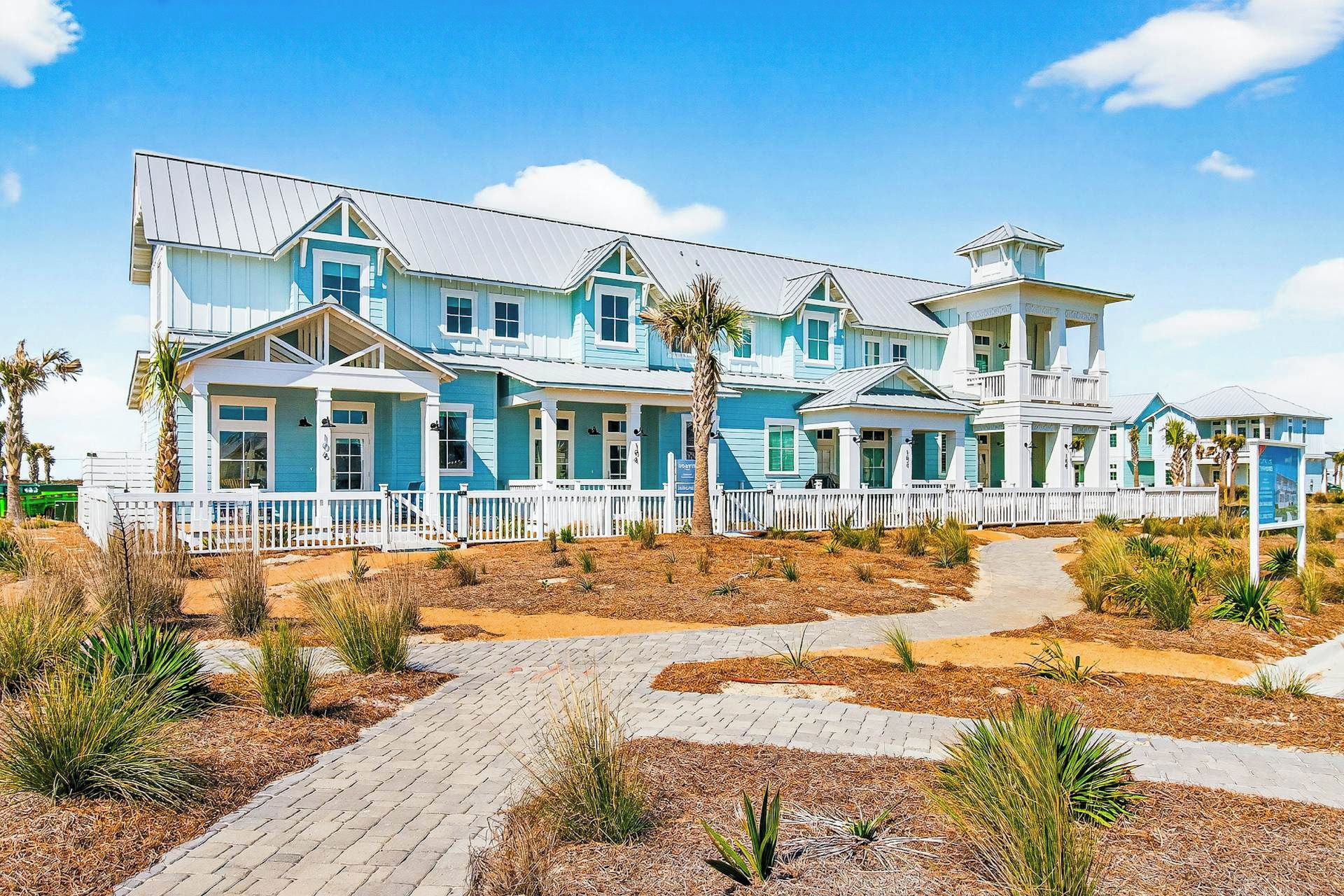 Una extensa propiedad frente a la playa, de varios pisos, con cerca de piquetes blancos, senderos pavimentados y jardines tropicales.
