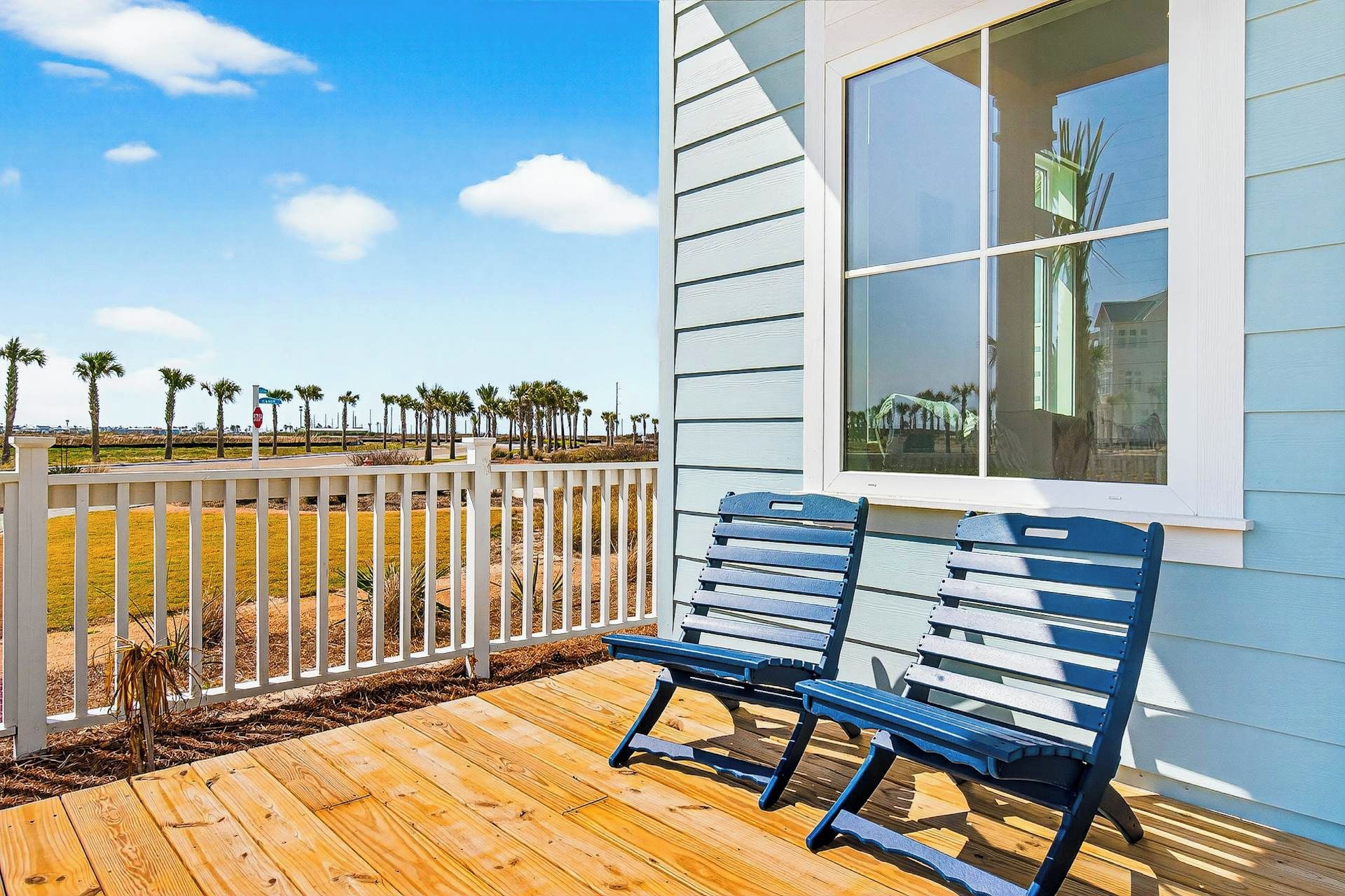 A wooden deck with two benches, a white fence, and a view of palm trees and a clear sky.