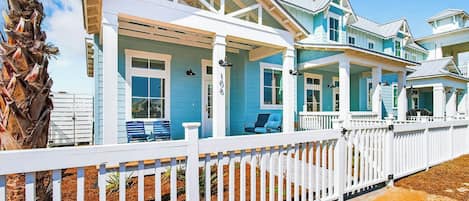 A coastal house with a white picket fence, multiple porches, and a clear view of the ocean.