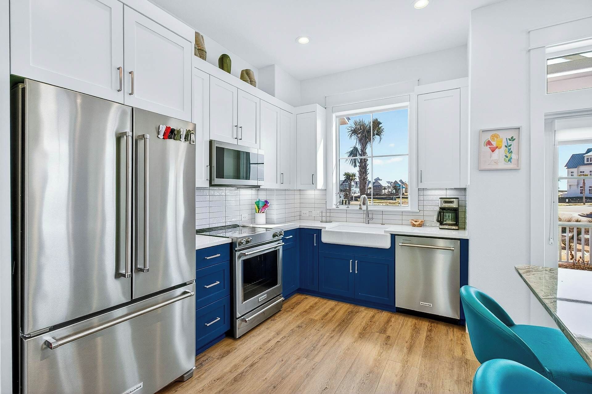 A modern kitchen with stainless steel appliances, blue cabinets, and a view of a residential area.