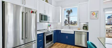 Une cuisine moderne dotée d’appareils électroménagers en acier inoxydable, de meubles bleus et offrant une vue sur un quartier résidentiel.